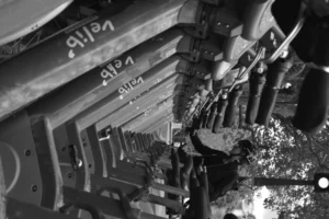 Cette photographie en noir et blanc montre une machine industrielle en action, probablement une scie mécanique ou un système de découpe. Le sujet principal est le mécanisme métallique en mouvement, avec des éclats de matériau projetés.La composition met en valeur les détails techniques et la précision mécanique. Le cadrage serré accentue les textures et les mouvements dynamiques. La lumière, bien que contrastée, révèle les contours nets des pièces métalliques. Les couleurs dominantes sont les nuances de gris, renforçant l’aspect industriel et brut.Le style est documentaire et technique, évoquant une ambiance de travail intense et mécanique.