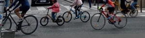 Cette photographie capture un **groupe de cyclistes** en mouvement, probablement lors d'une compétition ou d'une sortie collective. Le **sujet principal** est l'ensemble des coureurs, alignés et dynamiques.La **composition** est horizontale, mettant en valeur l'action et le rythme. Le **cadrage** serré et bas accentue la vitesse et l'énergie. La **lumière** semble naturelle, bien que légèrement contrastée, créant des ombres nettes.Les **couleurs dominantes** sont vives : rouges, noirs et blancs des tenues, avec des touches de rose et bleu. Le style est **sportif et dynamique**, évoquant une **ambiance compétitive et énergique**.