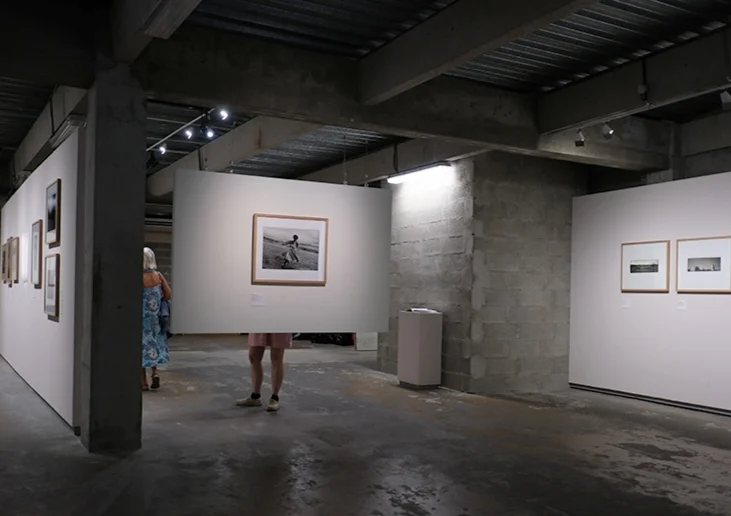 Dominique · 18/09/2026 · 731 x 516 Deux visiteurs dans une galerie d'art moderne observant des œuvres photographiques exposées sur des murs blancs et une paroi