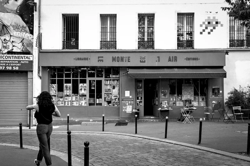 Thierry · 26/05/2024 · 3840 x 2560 Cette photographie en noir et blanc montre une boutique nommée **"Monte Air"** comme sujet principal. La composition met en valeur la façade du magasin, avec ses grandes vitrines exposant des marchandises et des enseignes.Le cadrage inclut une personne à gauche, partiellement visible, et une rue pavée menant vers l’entrée. La lumière est douce, créant des contrastes modérés et des ombres nettes. Les couleurs dominantes, bien que monochromes, suggèrent des tons gris et noirs, renforçant une ambiance rétro et intemporelle.Le style est documentaire, évoquant une scène urbaine calme et quotidienne. L’ambiance est sobre et légèrement nostalgique.