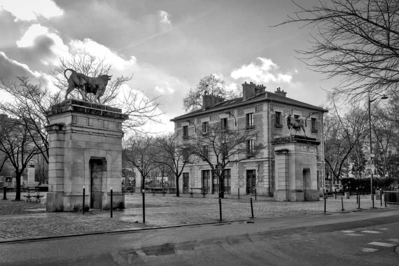 Thierry · 18/01/2024 · 3840 x 2563 Cette photographie en noir et blanc met en scène un imposant arc de triomphe et un bâtiment classique en arrière-plan, probablement une porte monumentale et une ancienne construction historique.La composition est symétrique, avec un cadrage large incluant une avenue et des arbres dénudés. La lumière, douce et diffuse, suggère un jour nuageux, accentuant les contrastes sans ombres marquées. Les tons gris dominent, renforçant l’aspect intemporel et solennel.Le style est documentaire et architectural, évoquant une ambiance historique et paisible, presque mélancolique.