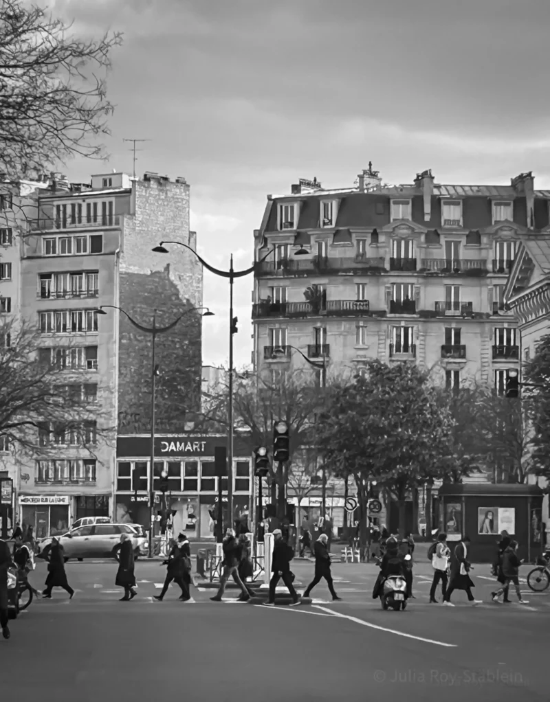 Thierry · 18/04/2024 · 3006 x 3840 Cette photographie en noir et blanc capture une scène urbaine animée. Le sujet principal est une rue parisienne avec une foule de passants traversant un carrefour. La composition met en valeur des immeubles haussmanniens typiques en arrière-plan, dont un avec une fresque murale stylisée.Le cadrage est large, incluant une perspective dynamique avec des lignes de fuite vers l’horizon. La lumière, douce et diffuse, accentue les contrastes sans être trop forte. Les couleurs dominantes, bien que monochromes, varient des gris clairs aux noirs profonds.Le style est documentaire et réaliste, évoquant une ambiance vivante et quotidienne dans un Paris historique.