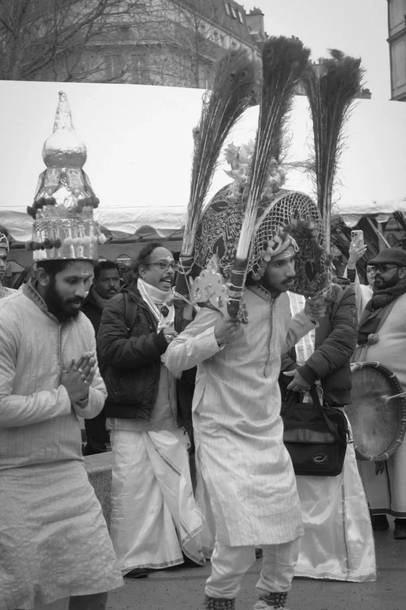 Thierry · 21/01/2024 · 2560 x 3840 Cette photographie en noir et blanc capture une scène religieuse traditionnelle. Le sujet principal est un homme au centre, vêtu de blanc, tenant des objets rituels (tridents et éventails). Autour de lui, d'autres participants, également en tenue traditionnelle, semblent participer à une cérémonie.La composition est dynamique, avec un cadrage serré sur les personnages. La lumière est douce, mettant en valeur les détails des vêtements et des accessoires. L'ambiance est solennelle et spirituelle, renforcée par les expressions et les gestes des participants. Le style est documentaire, reflétant une authenticité culturelle.