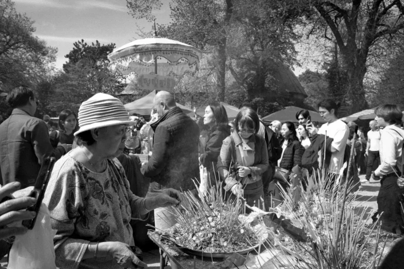 Thierry · 04/07/2025 · 3840 x 2560 Cette photographie en noir et blanc capture une scène de marché ou de foire artisanale. Le sujet principal semble être un groupe de personnes, dont certaines examinent des produits exposés sur des tables. La composition montre une foule animée, avec des tentes et des arbres en arrière-plan.Le cadrage est serré sur les interactions humaines, créant une ambiance conviviale. La lumière est naturelle, douce et diffuse, typique d’un jour ensoleillé mais sans contraste marqué. L’absence de couleurs renforce l’aspect intemporel et authentique de la scène, évoquant une ambiance chaleureuse et traditionnelle.