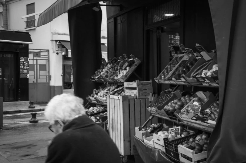 Thierry · 23/02/2024 · 3840 x 2560 Cette photographie en noir et blanc met en scène un vieil homme observant des étagères remplies d’objets divers, probablement des accessoires de pêche. Le sujet principal est son profil, capturé depuis l’extérieur d’un magasin.La composition est serrée, centrée sur les étagères et le client. Le cadrage est légèrement bas, créant une perspective immersive. La lumière est tamisée, avec des contrastes marqués entre ombres et clartés, renforçant l’ambiance intimiste et nostalgique. Le style est documentaire et réaliste, évoquant une scène du quotidien. L’absence de couleurs accentue les textures et les jeux d’ombres, renforçant une atmosphère à la fois mélancolique et authentique.