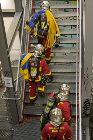 Thierry · 06/09/2025 · 2560 x 3840 Cette photographie montre un groupe de pompiers en tenue de protection, descendant un escalier métallique. Le sujet principal est l’équipe, vêtue de combinaisons colorées (jaune, rouge, bleu) et de casques de protection.La composition est dynamique, avec un cadrage serré sur les pompiers en mouvement. L’ambiance est professionnelle et tendue, évoquant une intervention d’urgence. Les couleurs dominantes sont vives et contrastées, attirant l’attention sur les équipements de sécurité. La lumière semble naturelle, bien répartie, mettant en valeur les détails des tenues et des visages. Le style est documentaire et réaliste.