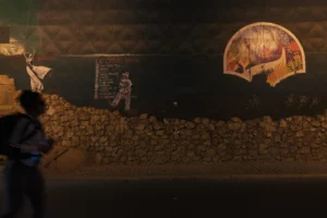 Thierry · 06/09/2025 · 3840 x 2560 Cette photographie montre une scène nocturne ou peu éclairée, probablement une œuvre artistique ou une installation.Le sujet principal semble être une silhouette humaine en contrebas, près d’un mur de pierres. En arrière-plan, une fresque ou une peinture murale représente une figure religieuse ou mythologique. Le cadrage est serré, mettant en valeur les contrastes entre ombre et lumière.Les couleurs dominantes sont des tons sombres et chauds, avec des éclairages dorés qui accentuent les détails. L’ambiance est mystérieuse et contemplative, évoquant une atmosphère à la fois dramatique et sacrée.
