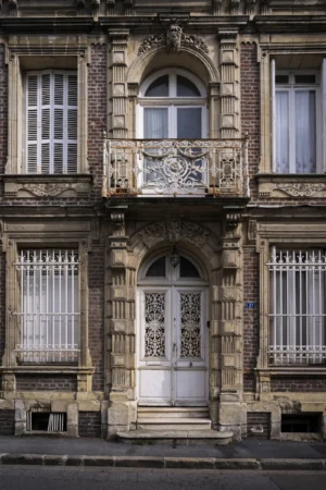 Thierry · 27/09/2025 · 2560 x 3840 Cette photographie met en valeur une façade architecturale ornée d'un style classique et ouvragé. Le sujet principal est une porte d'entrée élégante, entourée de décors sculptés et de motifs complexes.La composition est symétrique, avec des fenêtres alignées verticalement. Le cadrage est serré, centré sur la porte et les éléments décoratifs. La lumière, naturelle et douce, met en valeur les textures et les détails des sculptures. Les couleurs dominantes sont des tons neutres et gris-beige, rehaussés par des détails dorés et des contrastes subtils.L’ambiance est à la fois majestueuse et intemporelle, évoquant un héritage historique et artistique raffiné.