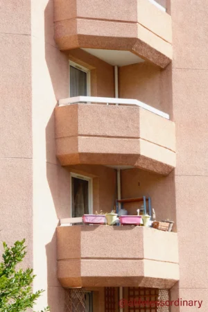 Cédric · 06/09/2025 · 2803 x 4205 Cette photographie montre la façade d’un immeuble avec trois balcons superposés. Le sujet principal est l’architecture et les balcons, dont l’un est équipé de pots de fleurs et d’une table.La composition est verticale, mettant en valeur la hauteur des balcons. Le cadrage est serré, centré sur les balcons et la partie inférieure de l’immeuble. La lumière semble naturelle, douce et légèrement tamisée, créant des ombres discrètes.Les couleurs dominantes sont des tons beiges et ocres pour l’immeuble, avec des touches de vert des plantes. Le style est épuré et moderne, évoquant une ambiance calme et résidentielle.