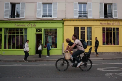 Alice · 13/09/2025 · 6223 x 4149 Cette photographie met en scène un couple à vélo comme sujet principal, au premier plan. La composition joue sur la profondeur avec les passants en arrière-plan devant deux bâtiments colorés, l’un vert et l’autre jaune, portant l’enseigne "Antoine & Lili".Le cadrage est serré sur les cyclistes, avec une perspective dynamique. La lumière est naturelle, légèrement tamisée, créant des ombres douces. Les couleurs dominantes sont vives et contrastées : vert, jaune, gris et noir.Le style est documentaire et urbain, capturant un moment de vie quotidienne. L’ambiance est vivante et animée, reflétant une scène typique d’une ville européenne.