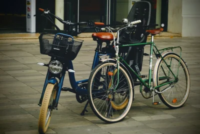 Denis · 13/09/2025 · 4898 x 3265 Cette photographie met en scène deux vélos stationnés côte à côte. Le sujet principal est un vélo électrique bleu avec panier avant, accompagné d’un vélo classique vert à l’arrière.La composition est symétrique et épurée, avec un cadrage serré sur les vélos. La lumière, tamisée et légèrement artificielle, crée des ombres douces, évoquant une ambiance nocturne ou crépusculaire. Les couleurs dominantes sont les teintes bleutées, vertes et grises, renforçant une atmosphère calme et moderne. Le style est sobre et urbain, tandis que l’ambiance, à la fois fonctionnelle et poétique, suggère une pause dans la ville.
