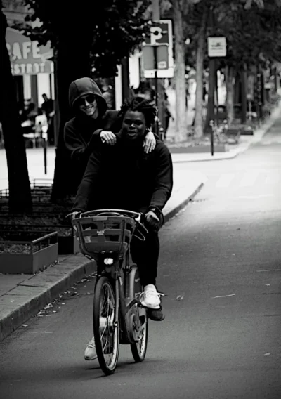 Denis · 13/09/2025 · 3357 x 4766 Cette photographie en noir et blanc met en scène un couple à vélo comme sujet principal. Le cadrage est serré, centré sur les deux personnes, avec un léger flou d’arrière-plan.La composition est dynamique, avec une ligne de fuite créée par la route et les arbres alignés. La lumière semble naturelle, douce, et crée des contrastes modérés. L’ambiance est intime et nostalgique, renforcée par le style rétro du cliché. Les couleurs dominantes, bien que monochromes, jouent sur les nuances de gris et de noir, accentuant l’émotion et la simplicité du moment.