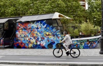 Deniz · 13/09/2025 · 5546 x 3560 Cette photographie met en scène un bus décoré de fresques colorées représentant des personnages de films et séries cultes. Le sujet principal est un cycliste passant devant ce bus.La composition est dynamique, avec un cadrage serré sur le vélo et le bus. La lumière est naturelle et semble provenir d’un jour ensoleillé. Les couleurs dominantes sont vives et variées, allant du bleu au rouge, en passant par des teintes pastel, créant un style pop-art et festif. L’ambiance est joyeuse et énergique, évoquant une célébration de la culture populaire.
