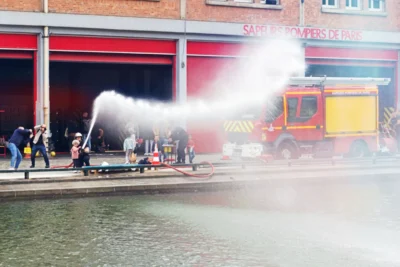 Fabienne · 13/09/2025 · 3840 x 2561 Cette photographie montre un **camion de pompiers** en action, projetant un puissant jet d’eau. Le **sujet principal** est l’intervention des secours, avec des pompiers et spectateurs en arrière-plan.La **composition** est dynamique, centrée sur le jet d’eau et le véhicule. Le **cadrage** est serré, mettant en valeur l’action. La **lumière** semble naturelle, bien que légèrement contrastée.Les **couleurs dominantes** sont les tons rouges (bâtiment), jaunes (véhicule) et gris (eau). L’**ambiance** est tendue et active, reflétant une situation d’urgence. Le style est documentaire, réaliste et immédiat.