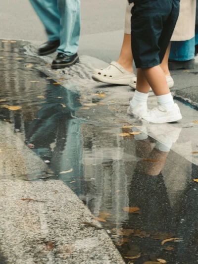 Seila · 13/09/2025 · 2880 x 3840 Cette photographie met en scène les pieds d’une personne en mouvement, vêtue de baskets blanches et de jeans. Le sujet principal est reflété dans une flaque d’eau, créant une symétrie visuelle.Le cadrage est serré, centré sur les pieds et leur reflet. La lumière semble naturelle, probablement en extérieur, avec des tons doux et légèrement contrastés. Les couleurs dominantes sont les gris (asphalte, eau), les bleus (jeans) et les blancs (baskets).Le style est simple et documentaire, évoquant une ambiance urbaine et spontanée, presque poétique grâce au jeu de miroir.