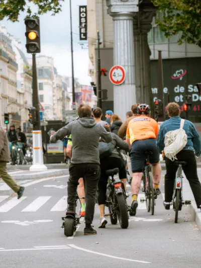 Seila · 13/09/2025 · 2880 x 3840 Cette photographie capture un groupe de cyclistes et de trottinetteurs traversant une intersection en ville. Le **sujet principal** est ce flux de personnes en mouvement, vu de dos.La **composition** est dynamique, avec un **cadrage serré** sur les individus, créant un effet de profondeur. La **lumière** est naturelle, légèrement voilée, suggérant un jour nuageux. Les **couleurs dominantes** sont neutres (gris, noir) avec des touches vives (orange, blanc) apportées par les vêtements et accessoires.Le **style** est documentaire et urbain, reflétant une **ambiance** active et moderne, typique d'une ville animée.