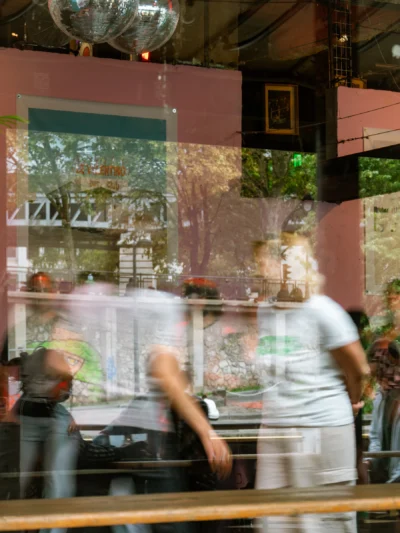 Seila · 13/09/2025 · 2880 x 3840 Cette photographie capture une scène floue et dynamique devant une vitrine de restaurant. Le **sujet principal** semble être un groupe de personnes en mouvement, suggérant une ambiance animée.La **composition** est déséquilibrée, avec un cadrage serré sur les passants et une partie de la vitrine. Les **couleurs dominantes** sont des tons chauds (rose, vert) et des contrastes vifs, accentués par la lumière naturelle et artificielle.Le **style** est réaliste et spontané, avec un effet de flou suggérant le mouvement. L’**ambiance** est urbaine et vivante, évoquant une rue animée, probablement en soirée.