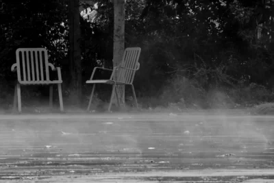 Vincent · 13/09/2025 · 3840 x 2564 Cette photographie en noir et blanc met en scène deux chaises de jardin vides, disposées sur une surface plane, probablement une terrasse ou un balcon. La composition est épurée, avec un cadrage serré qui isole les chaises et les place au centre. La lumière semble diffuse, créant une ambiance mystérieuse et légèrement mélancolique. Les contours sont flous, accentuant l'effet de brume ou de pluie légère.Les couleurs dominantes sont les nuances de gris, renforçant l'atmosphère contemplative et onirique. Le style rappelle le réalisme poétique, évoquant une solitude et une tranquillité presque intemporelle.