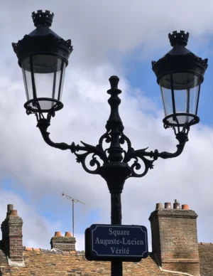 Laurence · 27/09/2025 · 2841 x 3677 Cette photographie met en scène un lampadaire ornemental ancien, sujet principal, avec ses deux lanternes stylisées. La composition montre aussi une plaque indiquant "Square Auguste-Lucien Vérité".Le cadrage est serré sur le lampadaire, avec un arrière-plan de bâtiments en pierre et un ciel partiellement nuageux. La lumière est naturelle, douce et diffuse, créant des ombres légères. Les couleurs dominantes sont les tons gris et noirs du métal et de la pierre, avec des touches bleutées dans le ciel.Le style est classique et historique, évoquant une ambiance paisible et intemporelle.