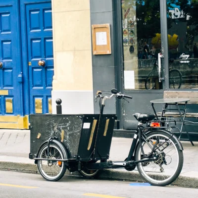 Laurence · 13/09/2025 · 2521 x 2520 Cette photographie met en scène un vélo-cargo moderne comme sujet principal. La composition est simple et épurée, centrée sur le vélo avec un cadrage serré.La lumière naturelle semble douce, éclairant uniformément la scène. Les couleurs dominantes sont les tons froids : bleu vif des portes, noir du vélo, et gris de la façade. Quelques touches chaudes, comme le jaune de la ligne au sol, apportent un contraste.Le style est urbain et contemporain, évoquant une ambiance moderne et fonctionnelle. L'image dégage une sensation de calme et d'efficacité, typique d'un environnement citadin dynamique.