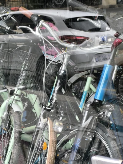 Laurence · 13/09/2025 · 3060 x 4080 Cette photographie montre un **parking à vélos** en intérieur ou semi-ouvert, avec des bicyclettes comme sujet principal. La **composition** est dense et désordonnée, avec des vélos entremêlés et des fils emmêlés.Le **cadrage** est serré, mettant en avant les détails des cadres et accessoires. La **lumière** semble artificielle, un peu froide, éclairant les objets sans ombres marquées. Les **couleurs dominantes** sont des tons neutres (gris, noir, bleu métallisé) avec des touches de vert et de blanc.Le style est **documentaire et réaliste**, reflétant une ambiance **urbaine et pratique**, voire un peu chaotique.