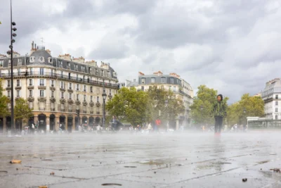 Claude · 5918 x 3945 Cette photographie capture une place urbaine sous la pluie. Le sujet principal est une fontaine en action, projetant de l’eau dans un ciel gris et nuageux. La composition montre des bâtiments haussmanniens typiques en arrière-plan, encadrant la scène.Le cadrage est large, incluant une partie du trottoir et de la rue mouillée. La lumière est tamisée par les nuages, créant une ambiance douce mais froide. Les couleurs dominantes sont les gris et les tons neutres, adoucis par les reflets de l’eau et les touches de vert des arbres. Le style est réaliste et documentaire, évoquant une atmosphère calme et mélancolique.