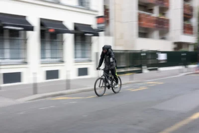 Claude · 5840 x 3893 Cette photographie met en scène un cycliste comme sujet principal, flou et en mouvement. La composition montre une rue urbaine avec des bâtiments en arrière-plan légèrement estompés.Le cadrage est serré sur le cycliste, avec une profondeur de champ réduite. La lumière semble naturelle mais diffuse, créant une ambiance un peu grise et neutre. Les couleurs dominantes sont des tons froids : gris, noir et quelques touches de blanc.Le style est dynamique, presque documentaire, avec une touche de flou artistique. L’ambiance est urbaine et moderne, évoquant le mouvement et la vie quotidienne dans une ville.