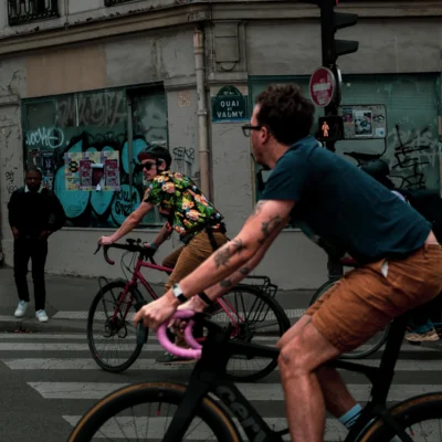 Jean-Paul · 13/09/2025 · 3000 x 3000 Cette photographie capture deux cyclistes en mouvement dans une rue urbaine. Le sujet principal est l’homme au premier plan, vêtu d’un t-shirt bleu et de lunettes, pédalant vigoureusement. La composition montre aussi une femme en combinaison colorée et un graffiti coloré en arrière-plan.Le cadrage est serré, mettant en valeur les cyclistes et leur environnement immédiat. La lumière est naturelle, légèrement contrastée, créant des ombres douces. Les couleurs dominantes sont vives : jaune, bleu, vert et rose, typiques d’un style urbain et dynamique. L’ambiance est énergique et moderne, reflétant la vie trépidante de la ville.