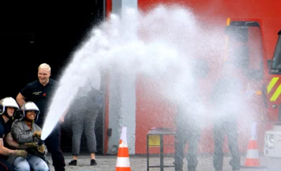 Pascale · 13/09/2025 · 2500 x 1518 Cette photographie montre des pompiers en action lors d’un exercice ou d’une intervention. Le sujet principal est un jet d’eau puissant dirigé vers un mur, avec plusieurs pompiers en tenue équipés de casques et masques.La composition met en valeur l’action dynamique, avec un cadrage serré sur les hommes et l’eau. La lumière est naturelle, bien répartie, sans ombres marquées. Les couleurs dominantes sont les tons rouges (mur, véhicule), gris (tenues), et blanc (vapeur d’eau).Le style est documentaire, réaliste, capturant une scène professionnelle. L’ambiance est intense et opérationnelle, reflétant l’urgence et la coordination.