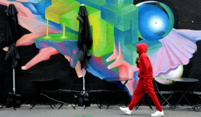Pascale · 13/09/2025 · 2500 x 1465 Cette photographie met en scène une personne en rouge marchant devant une fresque murale. Le sujet principal est cette silhouette contrastée, vêtue d’un manteau rouge vif.La composition joue sur le contraste entre le personnage et l’arrière-plan abstrait et coloré. Le cadrage est serré, centré sur la personne et le mur artistique.Les couleurs dominantes sont vives : rouge, bleu électrique, vert néon et noir. La lumière semble naturelle, bien que légèrement contrastée.Le style est urbain et moderne, mêlant art contemporain et vie quotidienne. L’ambiance est dynamique et légèrement futuriste.