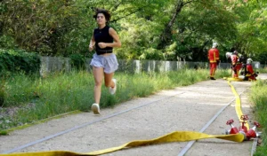 Pascale · 06/09/2025 · 700 x 410 Cette photographie capture une femme en train de courir, sujet principal, vêtue d’un short et d’un haut noirs. Elle franchit une ligne jaune au sol, symbolisant une arrivée ou un obstacle.La composition est dynamique, avec un cadrage serré sur la coureuse, mettant en valeur son mouvement. En arrière-plan, des arbres et des spectateurs ajoutent de la profondeur. La lumière est naturelle et douce, suggérant un jour ensoleillé.Les couleurs dominantes sont les verts de la végétation, le jaune vif de la ligne, et les tons neutres des vêtements. Le style est sportif et spontané, créant une ambiance énergique et motivante.