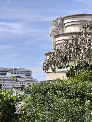 Laurence · 06/09/2025 · 3060 x 4080 Cette photographie met en scène un bâtiment avec une façade ornée de sculptures et de végétation retombante. Le sujet principal est la partie supérieure de l'édifice, où des statues et des plantes grimpantes créent un contraste organique et architectural.La composition est verticale, avec un cadrage serré sur les détails du bâtiment. La lumière est naturelle et douce, suggérant un jour ensoleillé. Les couleurs dominantes sont les verts des plantes, les tons beiges et gris de la pierre, et les bleus du ciel.Le style est à la fois classique et naturel, évoquant une harmonie entre art et nature. L’ambiance est paisible et élégante.