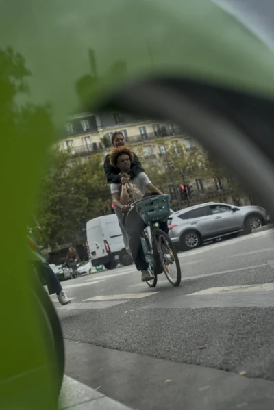 Ramón · 13/09/2025 · 1470 x 2200 Cette photographie montre une personne à vélo comme sujet principal, vue à travers un rétroviseur ou un objectif déformant. La composition est dynamique, avec un cadrage serré et légèrement flou, accentuant le mouvement. La lumière semble naturelle, mais un peu tamisée, typique d’un jour nuageux.Les couleurs dominantes sont des tons froids et neutres (gris, bleu pâle), adoucis par des touches de vert (végétation) et de blanc (véhicules). Le style est documentaire et spontané, capturant une scène urbaine du quotidien. L’ambiance est réaliste et légèrement mélancolique, reflétant le rythme effréné de la ville.