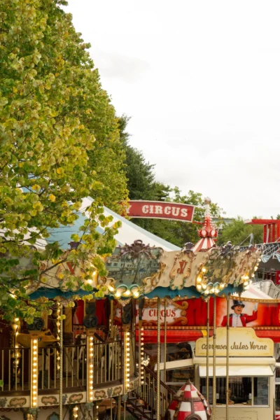 Renato · 13/09/2025 · 2560 x 3840 Cette photographie montre un carrousel de fête foraine comme sujet principal. La composition met en avant les chevaux de bois colorés et les structures ornées du manège, encadrés par des arbres feuillus.Le cadrage est serré, capturant les détails des sculptures et des éléments décoratifs. La lumière est douce et naturelle, probablement en journée, créant des ombres légères. Les couleurs dominantes sont les tons chauds : rouge, or et bois naturel, avec des touches de bleu et vert.Le style évoque une ambiance rétro et festive, typique des fêtes foraines traditionnelles, transmettant une sensation de nostalgie et de joie.