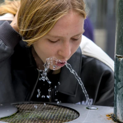 Thibault · 13/09/2025 · 3840 x 3840 Cette photographie montre une jeune femme comme sujet principal, penchée pour boire à un jet d’eau. Le cadrage est serré, centré sur son visage et ses mains.La composition est dynamique, avec un premier plan occupé par l’eau et un arrière-plan flou. La lumière semble naturelle et douce, mettant en valeur les détails du visage et les éclaboussures. Les couleurs dominantes sont des tons froids (bleu grisâtre de l’eau, noir du vêtement) contrastant avec les teintes chaudes de la peau.Le style est documentaire et spontané, créant une ambiance authentique et vivante.