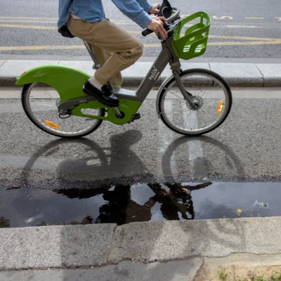 Thibault · 13/09/2025 · 3839 x 3839 Cette photographie montre un utilisateur de vélo électrique vert, probablement un service de location comme Lime ou Jump. Le sujet principal est le cycliste, partiellement visible, en mouvement sur une route.La composition joue sur la réflexion dans une flaque d’eau, créant un effet de symétrie et de duplication. Le cadrage est serré, centré sur le vélo et la flaque, avec un arrière-plan flou.Les couleurs dominantes sont le vert vif du vélo, les tons gris de la route et du trottoir, et les reflets bleutés de l’eau. La lumière semble naturelle, avec des ombres douces. Le style est réaliste et urbain, évoquant une ambiance dynamique et moderne.