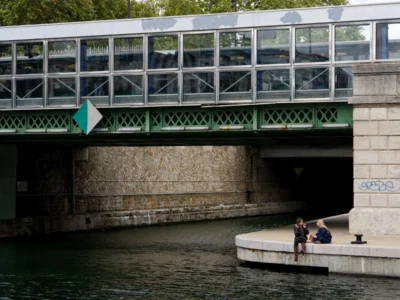 Cyrille · 13/09/2025 · 3840 x 2880 Cette photographie montre deux personnes assises sur une berge en béton, près d’un canal. Le sujet principal est ce duo en conversation, sous un pont métallique et vert.La composition est équilibrée, avec le pont en arrière-plan et les arbres en toile de fond. Le cadrage est serré sur les personnages et leur environnement immédiat. La lumière semble naturelle, avec des ombres douces.Les couleurs dominantes sont les verts du pont et de la végétation, les gris du béton et les bleus du canal. Le style est réaliste et documentaire, capturant une scène quotidienne. L’ambiance est calme et intimiste.