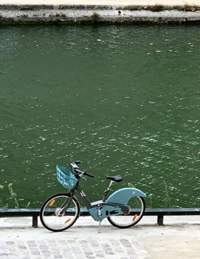Kerry · 13/09/2025 · 3022 x 3910 Cette photographie met en scène un vélo bleu clair, sujet principal, posé sur une bordure en béton près d’un plan d’eau vert émeraude. La composition est épurée, avec un cadrage serré sur le vélo et son reflet partiel dans l’eau. La lumière semble naturelle, douce, sans ombres marquées, créant une ambiance calme et apaisante. Les couleurs dominantes sont le bleu du vélo et le vert intense de l’eau, renforçant une sensation de fraîcheur. Le style est minimaliste et documentaire, évoquant une scène urbaine paisible et presque onirique.