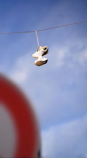 Franck T. · 04/10/2025 · 546 x 991 Cette photographie met en scène une **paire de tongs suspendue à un fil**. Le **sujet principal** est net et centré, tandis que l’arrière-plan est flou, créant un **cadrage contrasté**.La **composition** joue sur la profondeur de champ, isolant les tongs. La **lumière** naturelle, douce, éclaire le sujet sans ombre marquée. Les **couleurs dominantes** sont les tons pastel des tongs et le bleu du ciel, adoucis par une teinte rougeâtre en bas.Le style est **minimaliste et poétique**, évoquant une **ambiance mélancolique et onirique**.