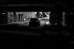 Claude · 5823 x 3882 Cette photographie met en scène un véhicule comme sujet principal, situé dans un tunnel urbain. La composition repose sur une perspective basse et centrale, avec des lignes architecturales convergentes.Le cadrage serré et profond accentue l'effet de profondeur. La lumière est faible et contrastée, créant une ambiance dramatique. Les couleurs dominantes sont les tons sombres de gris et noir, typiques d'un style noir et blanc.L'atmosphère est mystérieuse et immersive, renforcée par les jeux d'ombres et de clarté. Le style rappelle le photojournalisme ou une esthétique cinématographique.