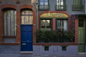 Thierry · 04/10/2025 · 3840 x 2560 Cette photographie met en scène une façade urbaine avec une porte bleue comme sujet principal. La composition est symétrique, centrée sur la porte numérotée 15, entourée de bâtiments en briques rouges.Le cadrage est serré, mettant en valeur les détails architecturaux et les jeux de lumière. Les couleurs dominantes sont les tons rouges des briques, le bleu de la porte, et les touches de vert des plantes grimpantes.La lumière naturelle, douce et légèrement tamisée, crée une ambiance calme et chaleureuse. Le style évoque un charme résidentiel européen, typique des quartiers historiques.