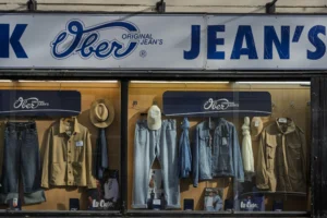 Thierry · 04/10/2025 · 3840 x 2560 Cette photographie montre une vitrine de magasin de vêtements, plus précisément une boutique de jeans "Lee Original Jean’s". Le sujet principal est l'étalage de divers jeans et vestes suspendus.La composition est symétrique, avec des vêtements bien alignés. Le cadrage est serré sur la vitrine, mettant en valeur les produits. La lumière est douce et naturelle, éclairant uniformément les vêtements.Les couleurs dominantes sont les bleus (tons de jeans) et les gris, avec des touches de blanc et de noir. Le style est épuré et professionnel, évoquant une ambiance rétro et classique. L'ensemble dégage une impression de qualité et de tradition.