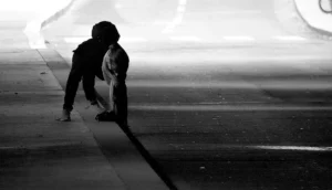 Franck T. · 18/10/2025 · 1000 x 572 Cette photographie en noir et blanc met en scène un sujet principal : une personne assise sur le bord d'une route, accompagnée d'un chien. La composition est épurée, centrée sur cette scène intime. Le cadrage est serré, capturant uniquement les deux protagonistes et une partie de l’asphalte et du trottoir.La lumière, douce et contrastée, accentue les ombres et crée une ambiance mélancolique. Les couleurs dominantes sont les nuances de gris, renforçant l’aspect dramatique et poétique. Le style est sobre et réaliste, évoquant une atmosphère de solitude et de calme.