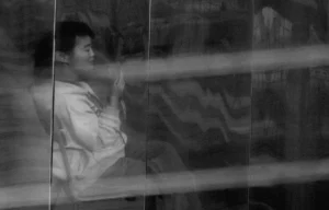Franck T. · 18/10/2025 · 1000 x 640 Cette photographie en noir et blanc met en scène un homme comme sujet principal, partiellement visible à travers une vitre striée. La composition joue sur la transparence et les reflets, créant une ambiance mystérieuse et fragmentée. Le cadrage serré et légèrement flou accentue l'effet de profondeur et d'isolement.Les traits sont adoucis par la lumière douce et diffuse, renforçant une atmosphère contemplative et mélancolique. Les couleurs, limitées au noir, blanc et gris, soulignent les contrastes et les textures. Le style rappelle une approche artistique et introspective, évoquant une émotion subtile et intime.