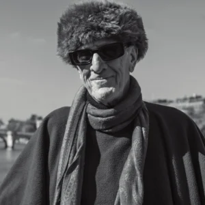 Don · 11/10/2025 · 4672 x 4672 Cette photographie met en scène un homme âgé comme sujet principal, vêtu d’un manteau sombre, d’un foulard et d’un chapeau à fourrure, avec des lunettes de soleil. Le cadrage est serré, centré sur son visage, créant une ambiance intime.La lumière, naturelle et contrastée, accentue les ombres et les textures, donnant un rendu dramatique. Les couleurs dominantes sont les tons de gris et noir, renforçant l’aspect monochrome et cinématographique. Le style rappelle le photojournalisme ou le portrait documentaire, évoquant une atmosphère à la fois sobre et expressive, presque mélancolique.