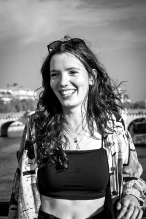 AnJo · 11/10/2025 · 1280 x 1920 Cette photographie met en scène une jeune femme comme sujet principal, souriante, avec des cheveux longs et bouclés. Le cadrage est serré, centré sur elle, avec un arrière-plan flou montrant un paysage urbain.La lumière est naturelle, douce et légèrement latérale, créant des contrastes subtils. La photo est en noir et blanc, ce qui accentue les textures et les jeux d'ombres.Le style est simple et spontané, évoquant une ambiance détendue et joyeuse, presque documentaire. Les tons clairs et foncés renforcent l’émotion et la chaleur du moment.