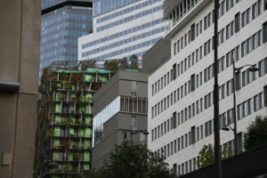 Pierre · 18/10/2025 · 6048 x 4024 Cette photographie montre des bâtiments urbains modernes. Le sujet principal est un immeuble blanc aux fenêtres alignées, partiellement caché par un autre édifice plus ancien à gauche.La composition met en valeur la juxtaposition entre l’architecture contemporaine et traditionnelle. Le cadrage est serré, centré sur les façades, avec une légère inclinaison vers le haut.La lumière est naturelle, légèrement diffuse, créant des contrastes doux. Les couleurs dominantes sont les tons gris, blancs et verts (balcons végétalisés). Le style est réaliste et documentaire, évoquant une ambiance urbaine contemporaine et dynamique.