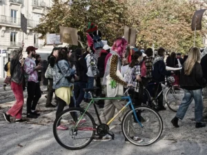 Cyrille · 11/10/2025 · 1200 x 900 Cette photographie montre un groupe de personnes participant à une manifestation ou un rassemblement festif. Le sujet principal est une femme sur un vélo décoré de guirlandes et de banderoles colorées.La composition est dynamique, avec des participants en mouvement autour du vélo. Le cadrage est serré, mettant en valeur les visages et les détails des accessoires. La lumière semble naturelle, légèrement diffuse, créant des ombres douces. Les couleurs dominantes sont vives et variées, avec des tons pastel et des touches de rose et bleu.L’ambiance est joyeuse et engagée, reflétant une énergie collective et festive.