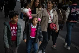 Muriel · 18/10/2025 · 2048 x 1378 Cette photographie capture un groupe de quatre personnes en mouvement, probablement dans un lieu public. Le sujet principal semble être les trois enfants et l’adulte qui les accompagne.La composition montre une dynamique de marche, avec un cadrage serré sur les visages et les détails vestimentaires. La lumière est naturelle, légèrement tamisée, créant des ombres douces. Les couleurs dominantes sont sobres : gris, noir, rose et bleu, apportant une ambiance réaliste et quotidienne.Le style est documentaire, reflétant une scène de vie authentique et spontanée. L’ambiance est calme et familiale, malgré le mouvement.