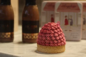 Francoise · 05/10/2025 · 6000 x 4000 Cette photographie met en scène un petit gâteau recouvert d’un chapeau en sucre rose bonbon, posé sur une surface blanche. Le sujet principal est ce gâteau décoratif, évoquant un style sucré et ludique.La composition est simple et centrée, avec en arrière-plan deux bouteilles de sauce et une boîte de biscuits, suggérant un contexte culinaire. Le cadrage est serré, mettant l’accent sur le détail du chapeau.La lumière est douce et naturelle, créant des ombres légères. Les couleurs dominantes sont le rose vif, le beige et le marron, apportant une ambiance chaleureuse et festive. Le style est photographique et délicat, évoquant la gourmandise et la créativité.